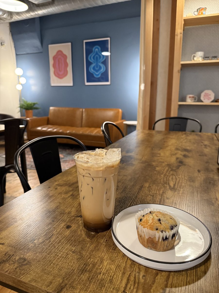An iced coffee and a muffin on a wooden table in the blue back room, a leather couch behind