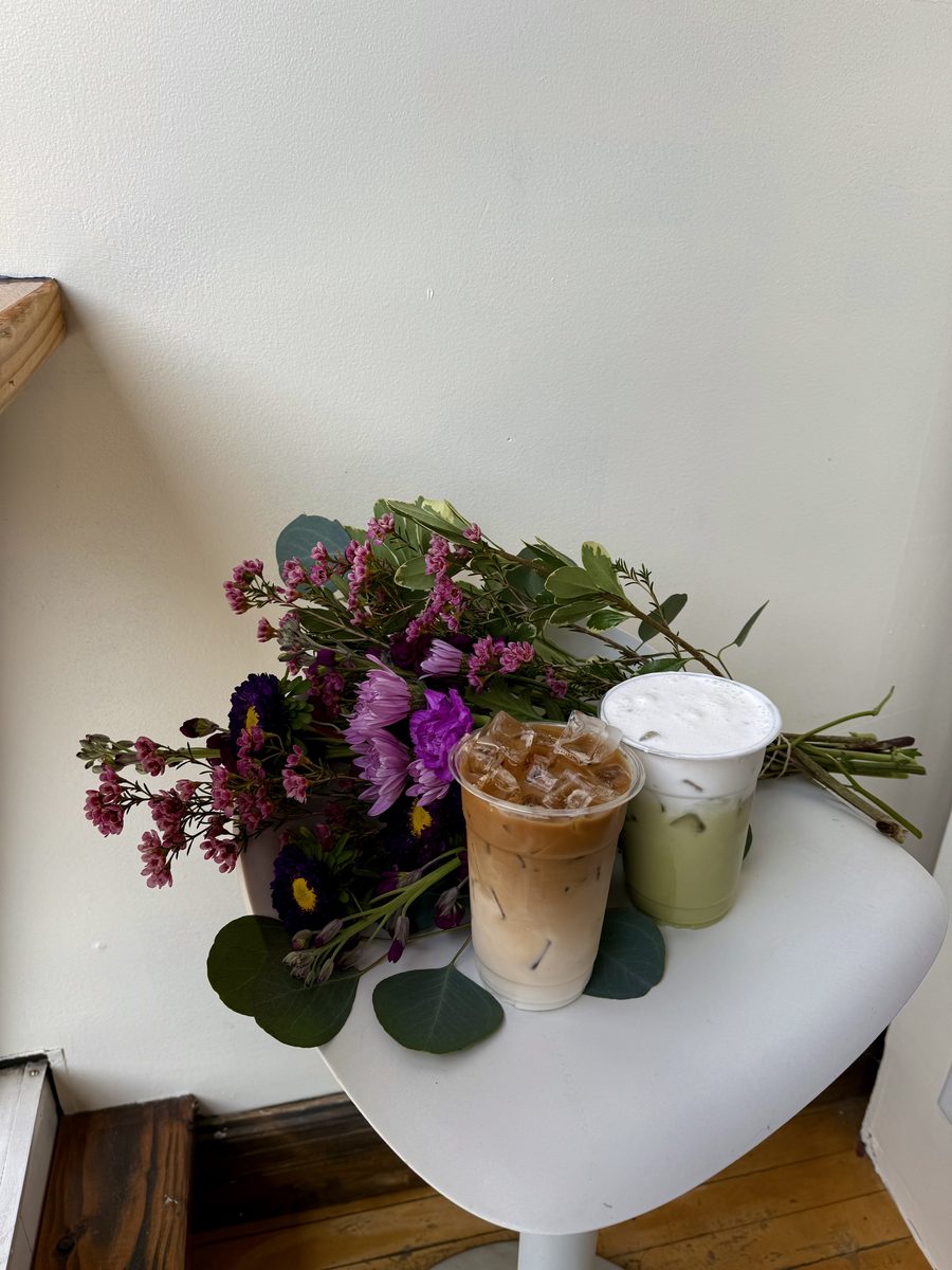 An iced coffee and an iced matcha on a white table next to a vase of flowers